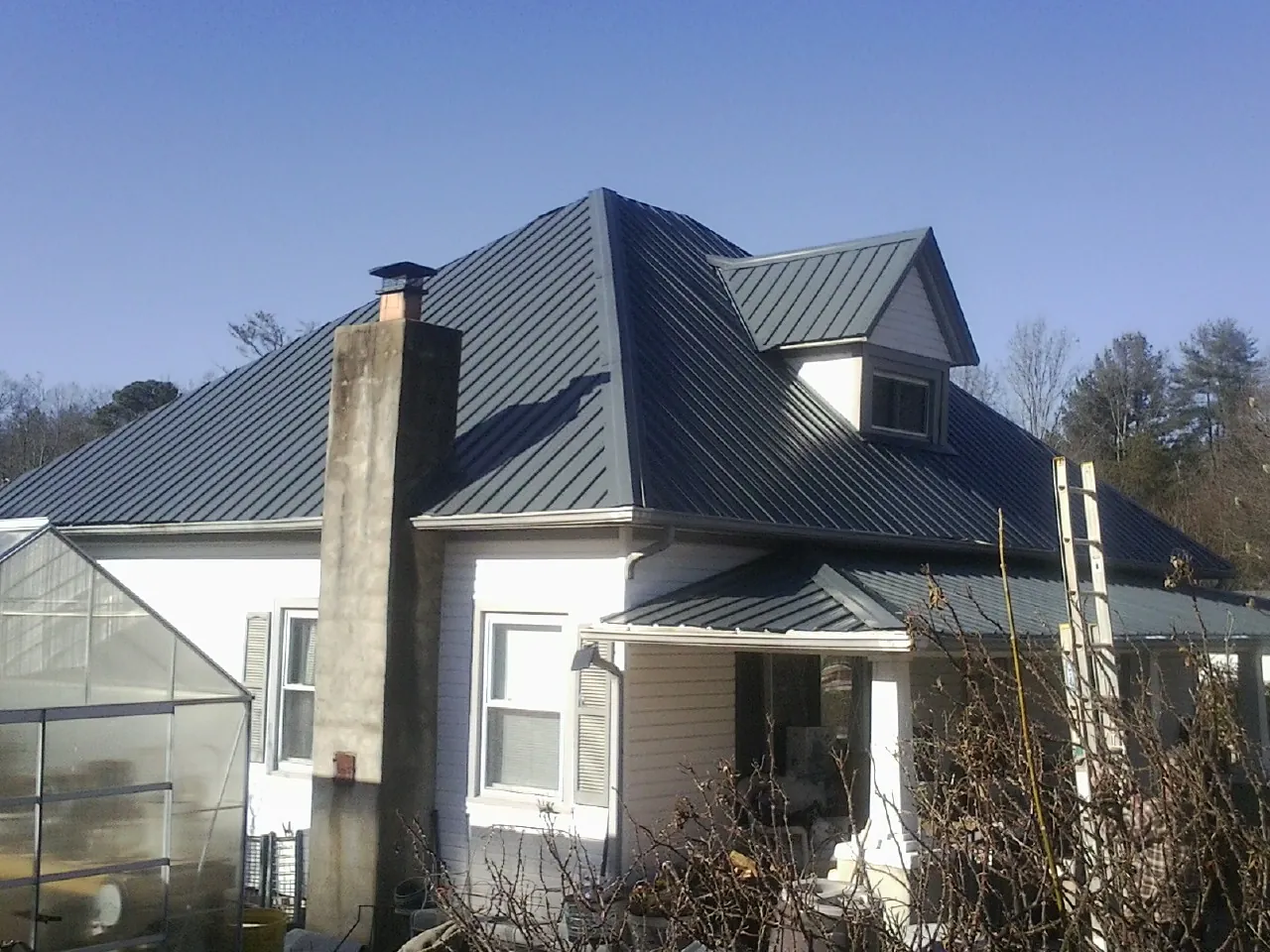 Dark blue standing seam metal roof on a white farmhouse with dormer — Slate & Tile Roof Repair by Roofing Brothers in Limon
