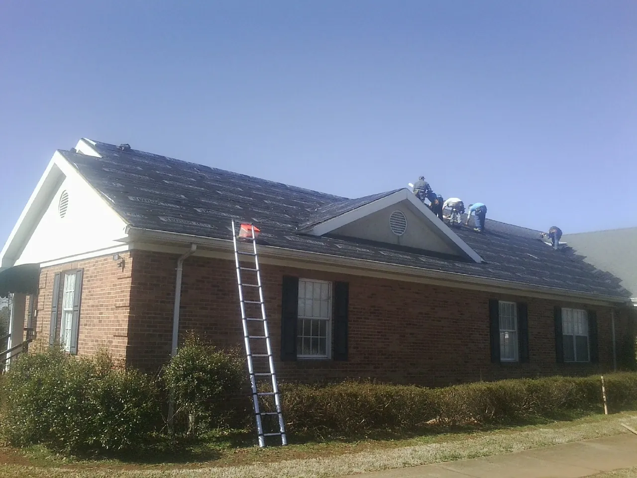 Crew tearing shingles off a brick ranch roof with a ladder set — Metal Roof Repair work by our crew in Limon
