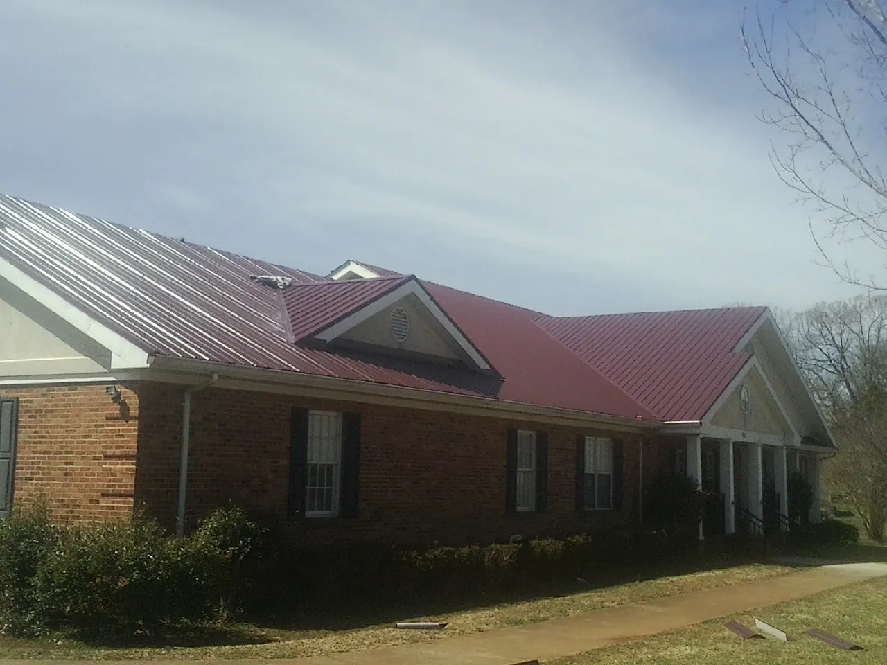 Red metal roof with gabled entries on a long brick building, from a Hail Damage Roof Repair job in Limon