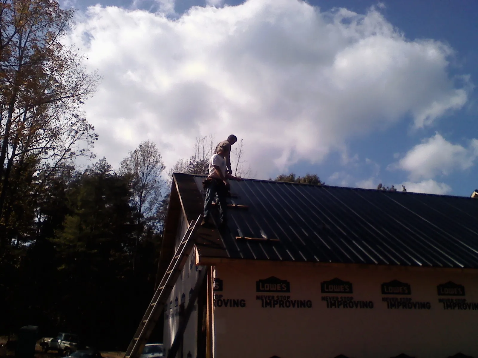 Roofer fastening dark metal panels high against a cloudy sky, from a Roof Inspection job in Limon